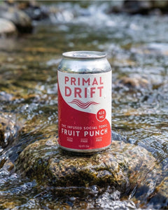 A can of Fruit Punch Social Tonic, an alcohol-free THC-infused drink, rests on a wet rock in a stream, surrounded by flowing water and softly blurred natural scenery in the background.