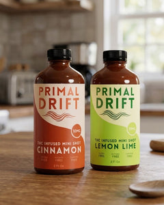 Two bottles of Primal Drift THC-infused mini shots on a wooden surface with a kitchen background.